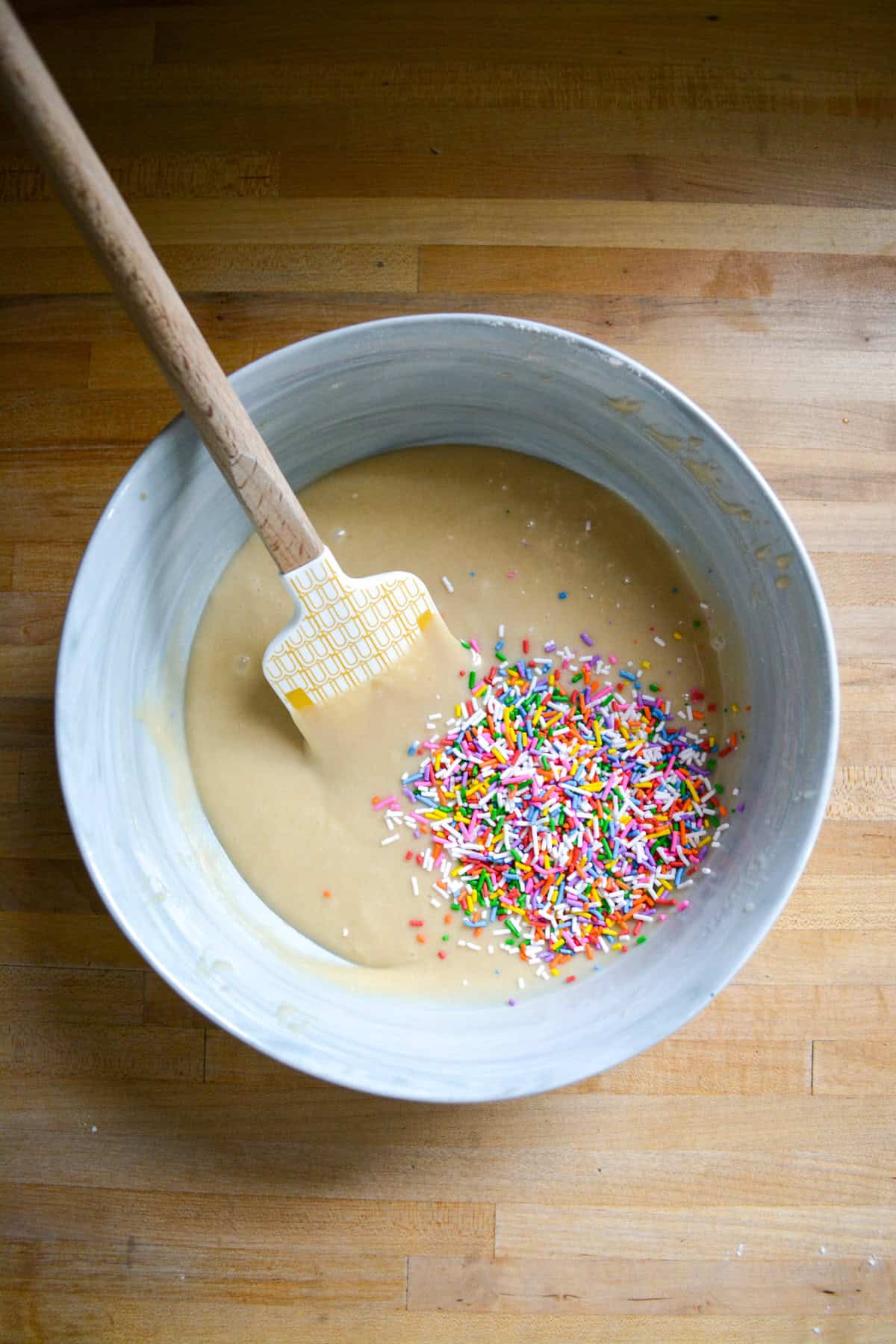 Sprinkles added into cupcake batter in a large bowl with a spatula inside.