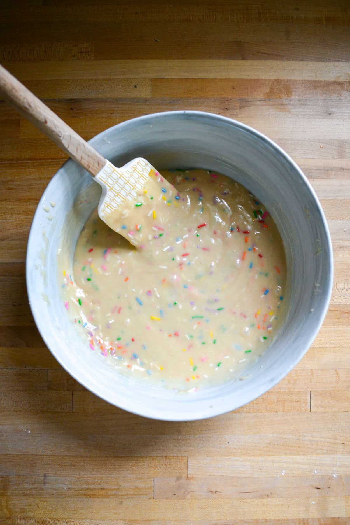 Rainbow sprinkles mixed into cupcake batter in a large bowl.