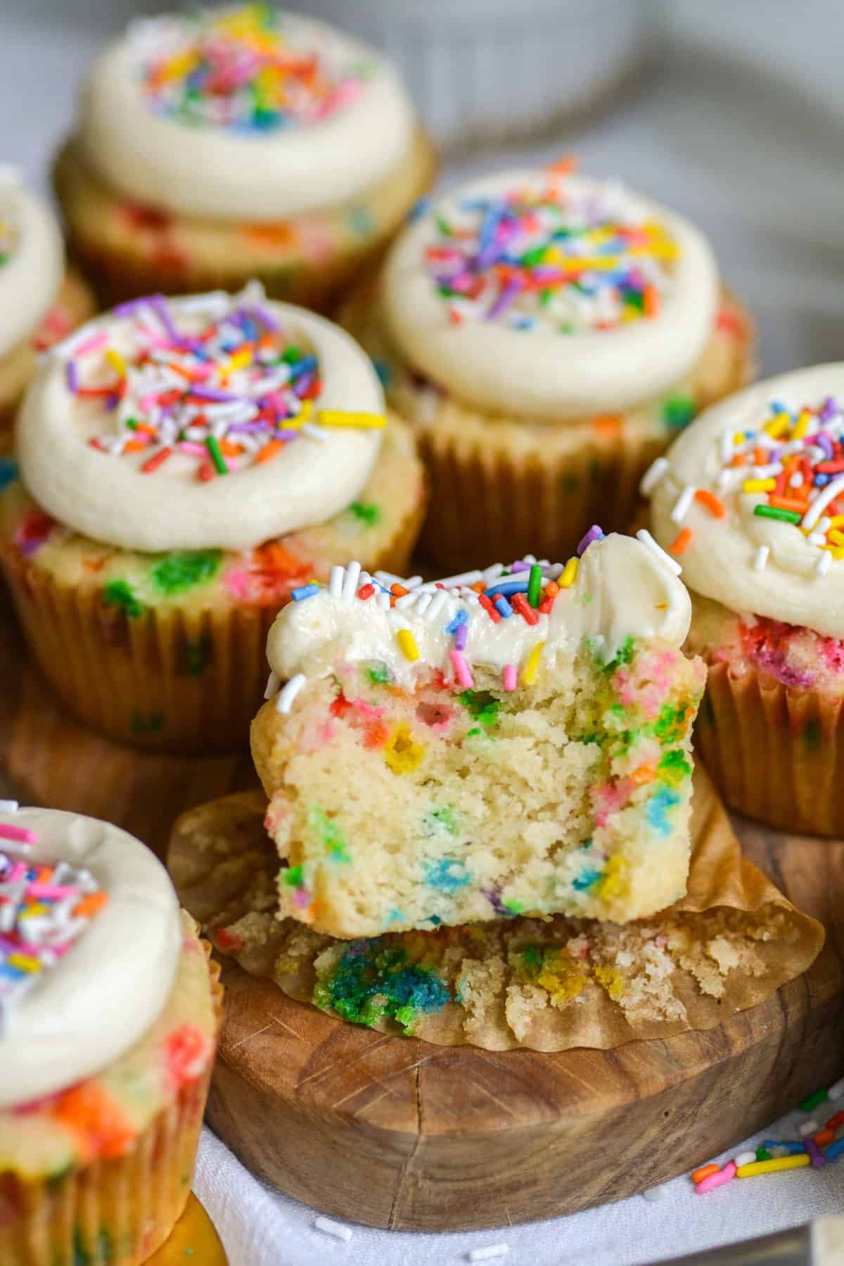 Vegan Funfetti cupcake with a bite taken out of it on a small board with other cupcakes on it.