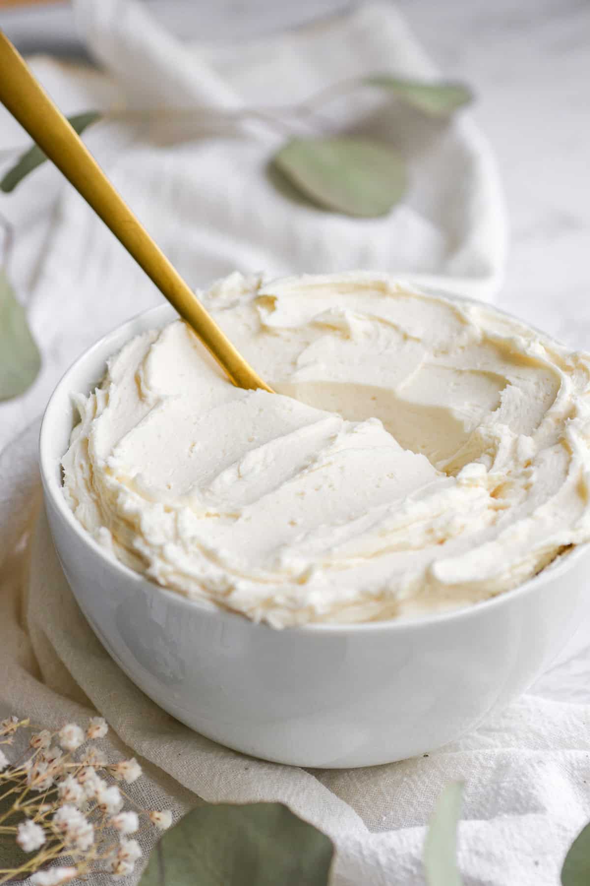 Vanilla frosting in a small bowl with a gold spoon in it.