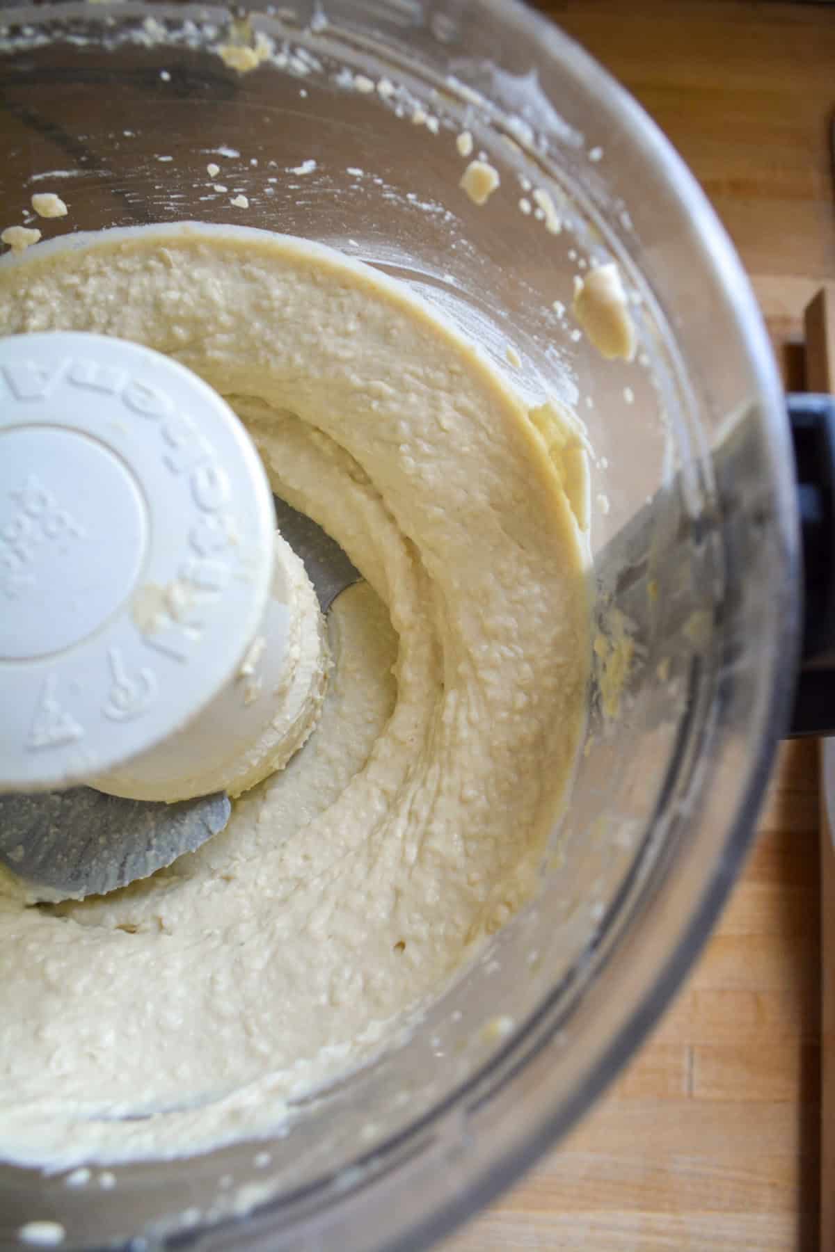 Hummus blended smooth in the bowl of a food processor.