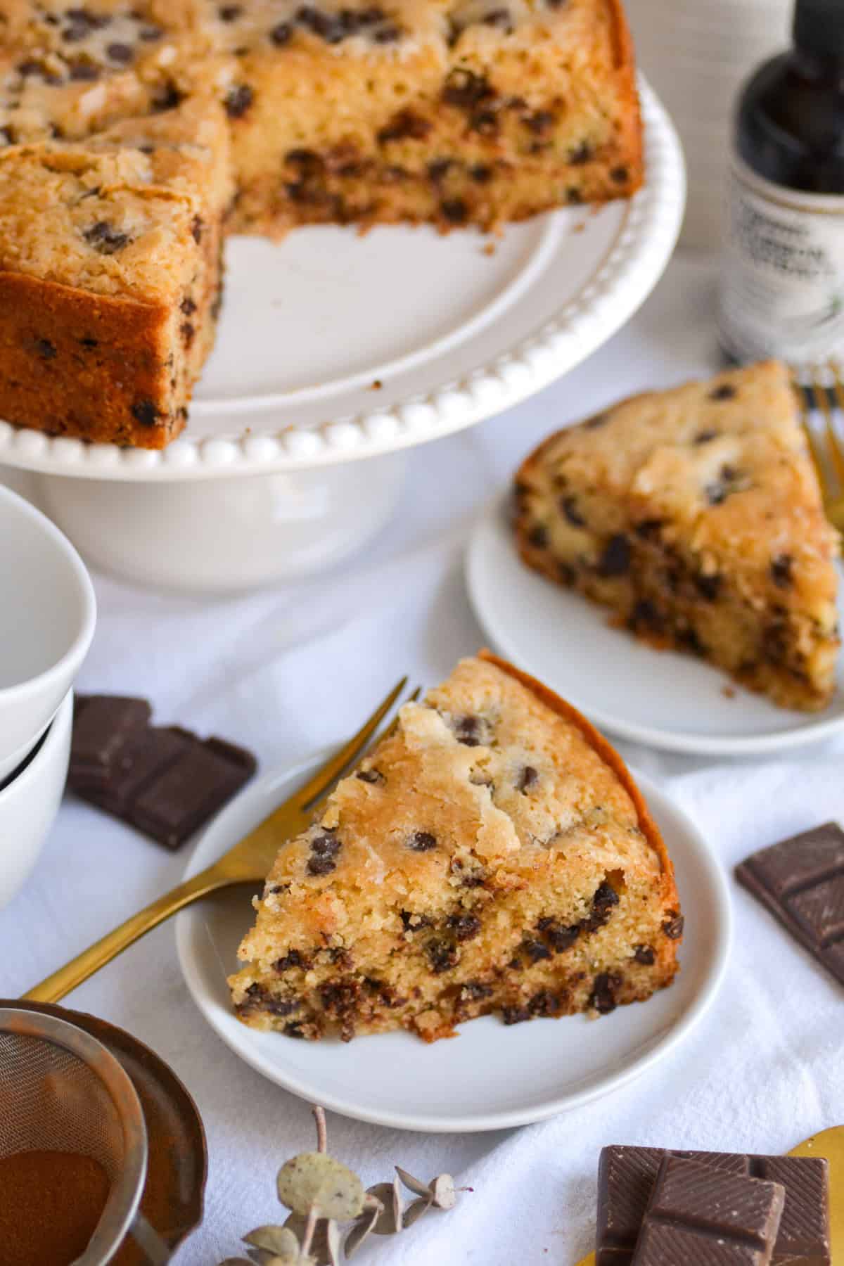Two slices of chocolate chip snack cake on small plates with the remaining cake on a cake stand in the background.