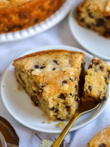 A slice of chocolate chip snack cake on a plate with a bite taken out of it.