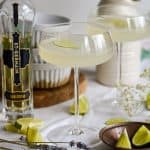 A French Gimlet in a coupe glass with a bottle of elderflower liqueur next to it.