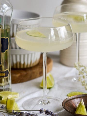 A French Gimlet in a coupe glass with a bottle of elderflower liqueur next to it.