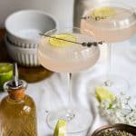 Two Lavender Gimlets in glasses on a linen cloth with a bottle of lavender syrup in the scene.