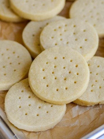 Vegan Shortbread Cookies layered on top of each other on a parchment-lined baking sheet.