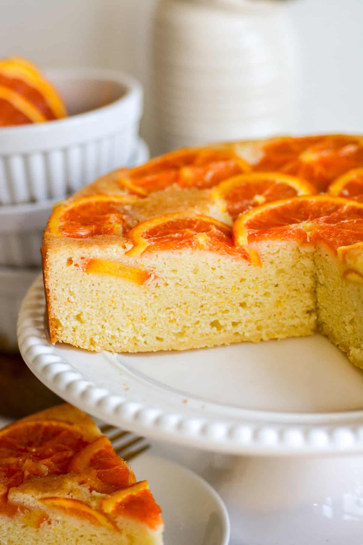 Vegan Orange Upside Down Cake on a cake stand with slices taken out of it.