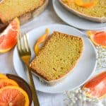 Vegan Orange Cardamom Loaf Cake slice on a small plate with orange wedges in the scene.