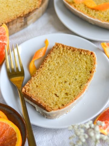 Vegan Orange Cardamom Loaf Cake slice on a small plate with orange wedges in the scene.