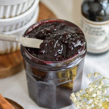 A knife inside a glass jar of cherry jam.