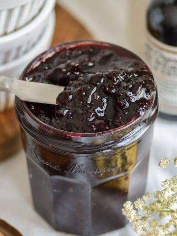 A knife inside a glass jar of cherry jam.