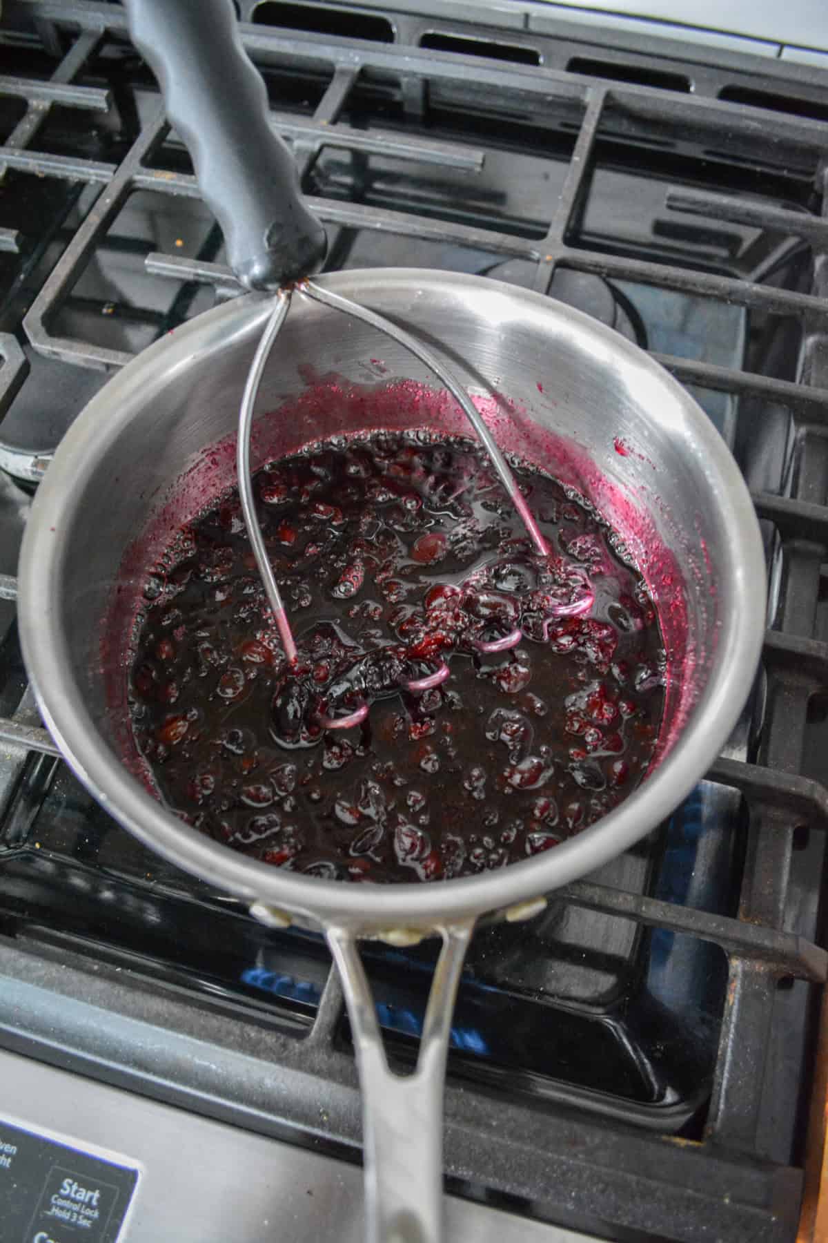 A potato masher breaking up the cherries in a saucepan.