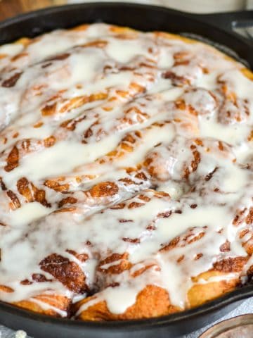 Cinnamon Roll Focaccia drizzled with sweet vanilla glaze in a cast iron pan.