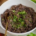 Refried Black Beans topped with cilantro in a bowl with a gold spoon.