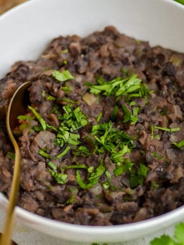 Refried Black Beans topped with cilantro in a bowl with a gold spoon.