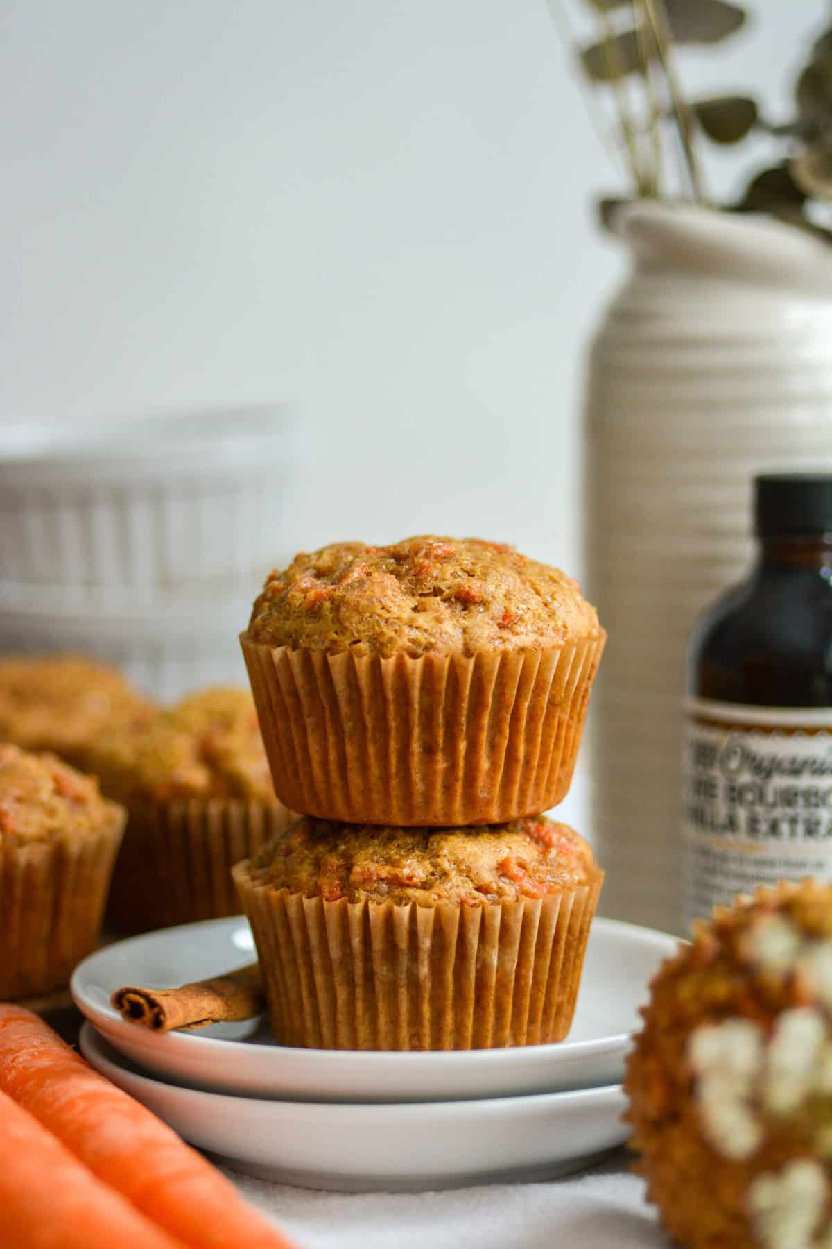 Two Vegan Carrot Muffins stacked on top of each other on a white plate.