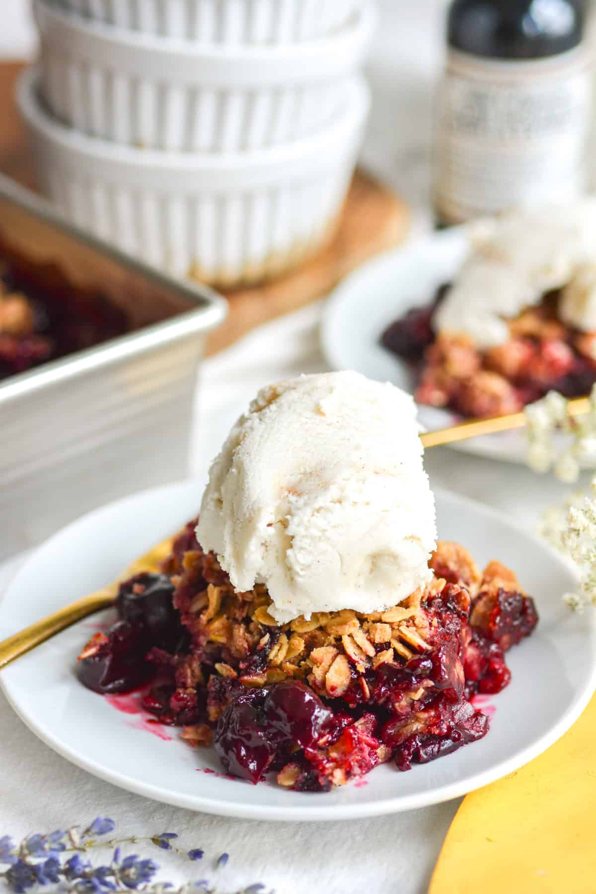 A scoop of cherry crisp with frozen cherries on a plate topped with a scoop of ice cream.