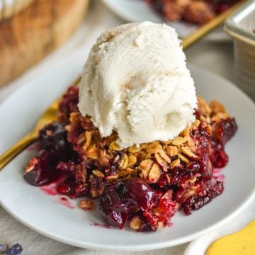 A scoop of cherry crisp with frozen cherries on a small plate topped with a scoop of ice cream.
