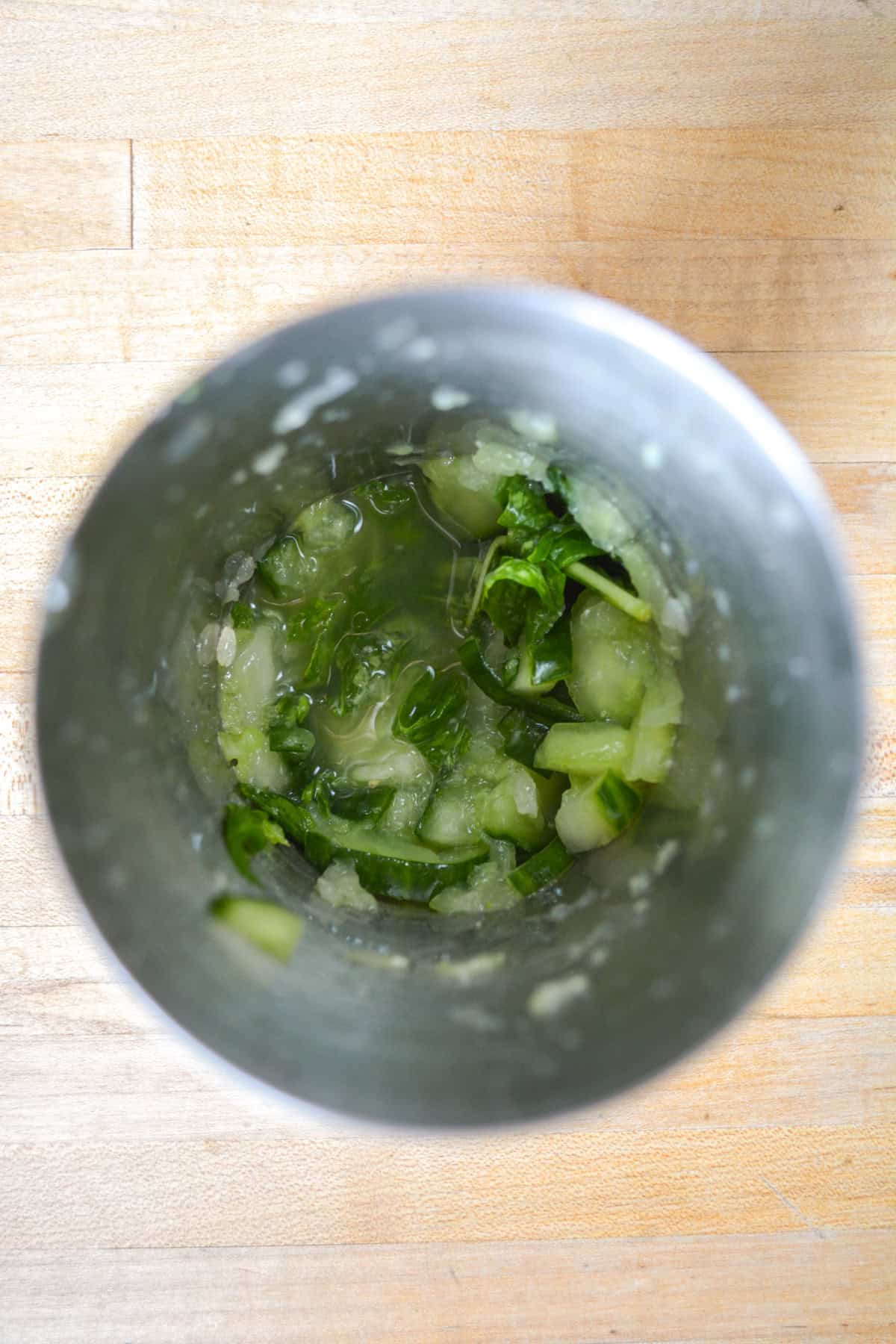 Muddled cucumber and basil in a cocktail shaker.