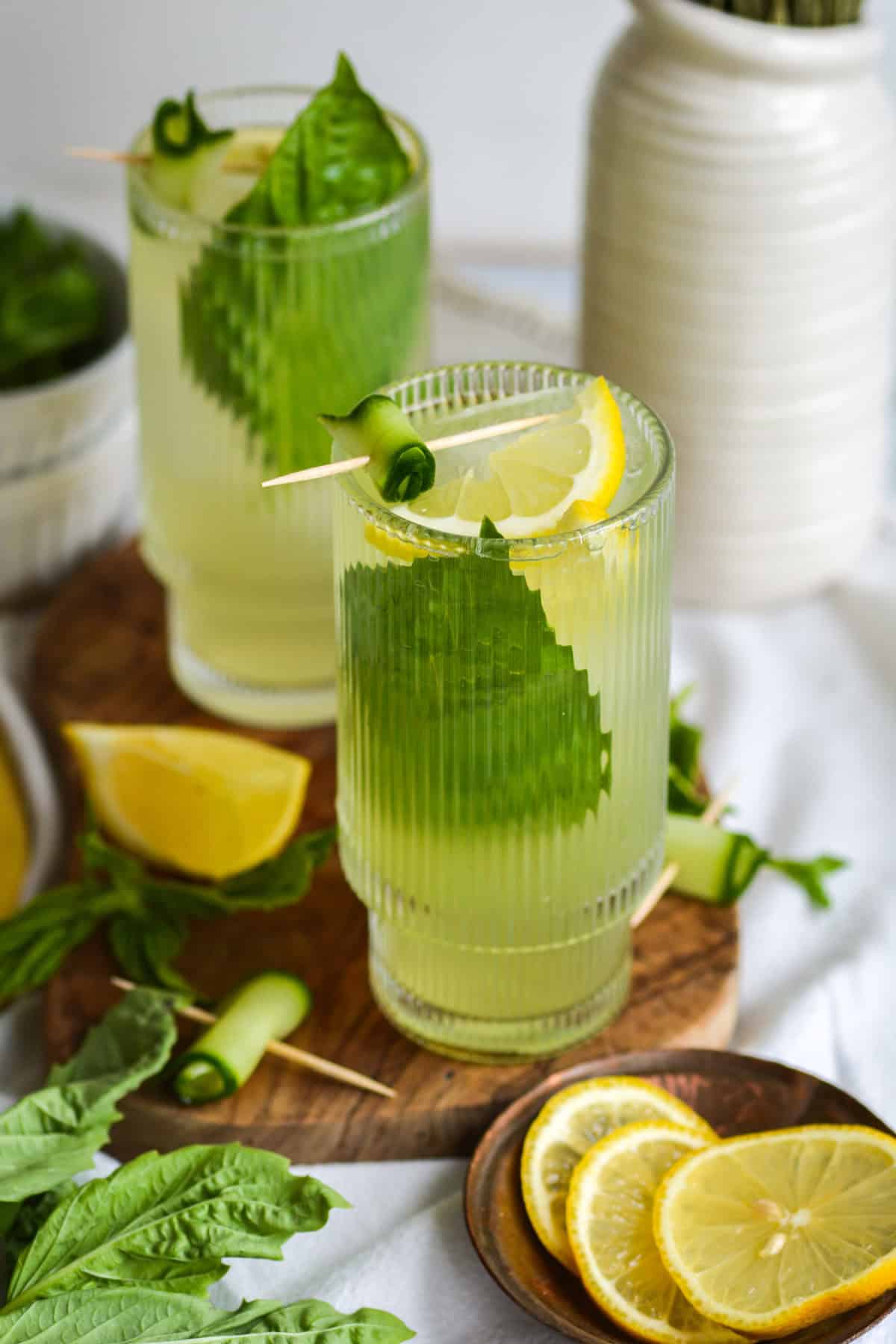 2 glasses of Cucumber Basil Mocktail garnished with basil on a wooden board.