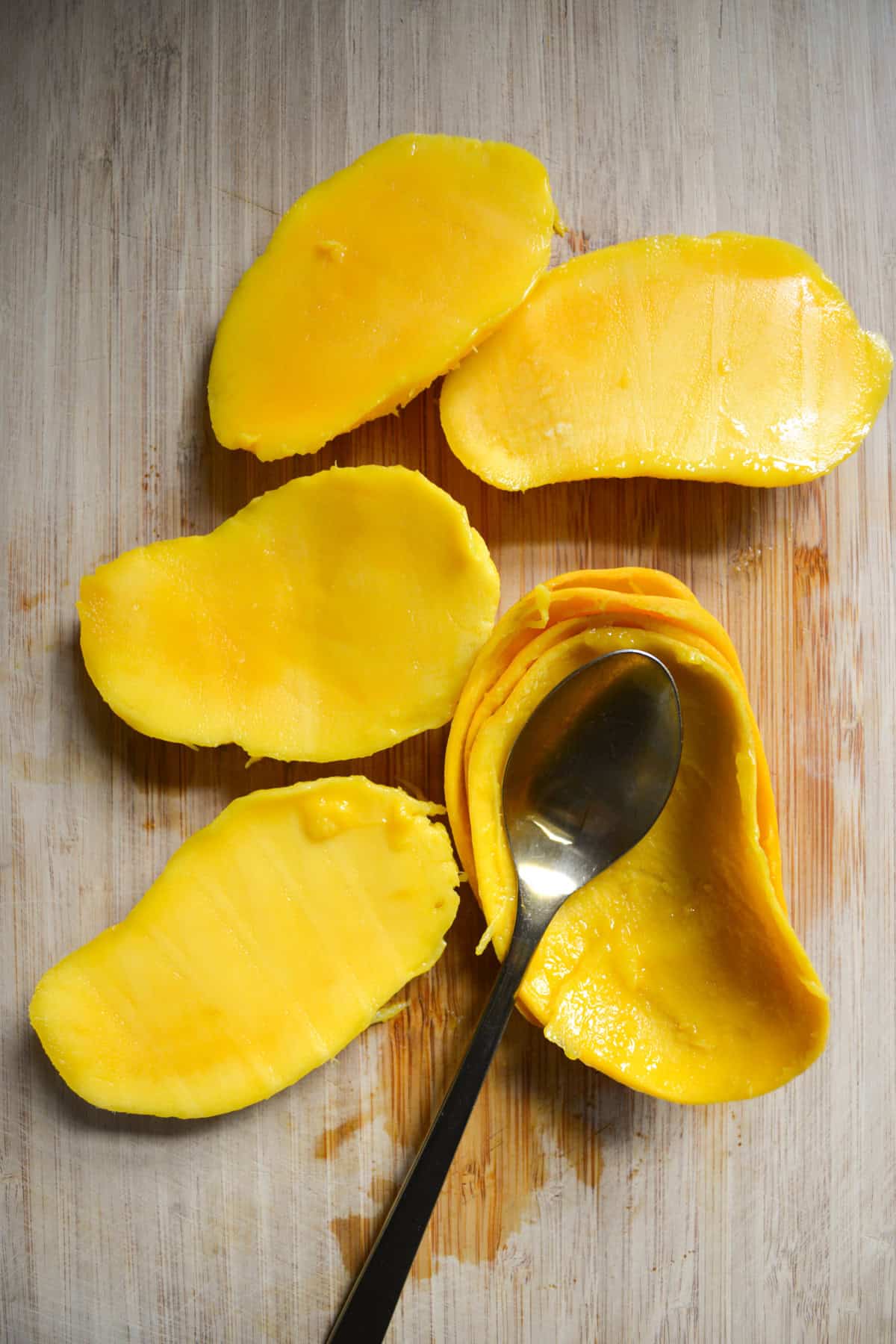 Mango cheeks that have been scooped out of the skin on a wooden cutting board.