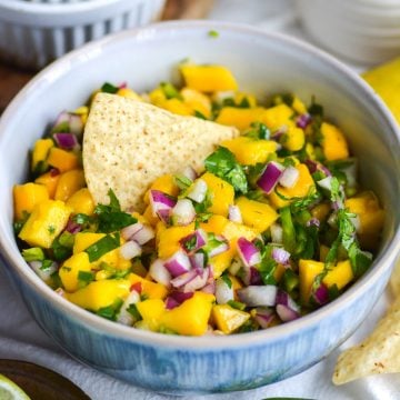 Mango Pico de Gallo in a bowl with a tortilla chip stuck into the salsa.