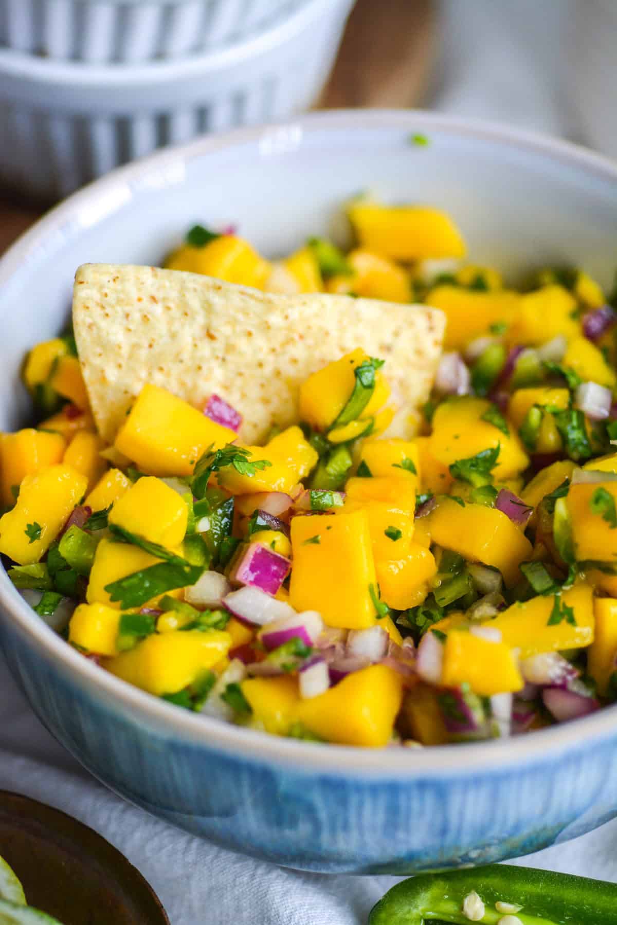 Mango Pico de Gallo in a blue bowl with a tortilla chip in it.