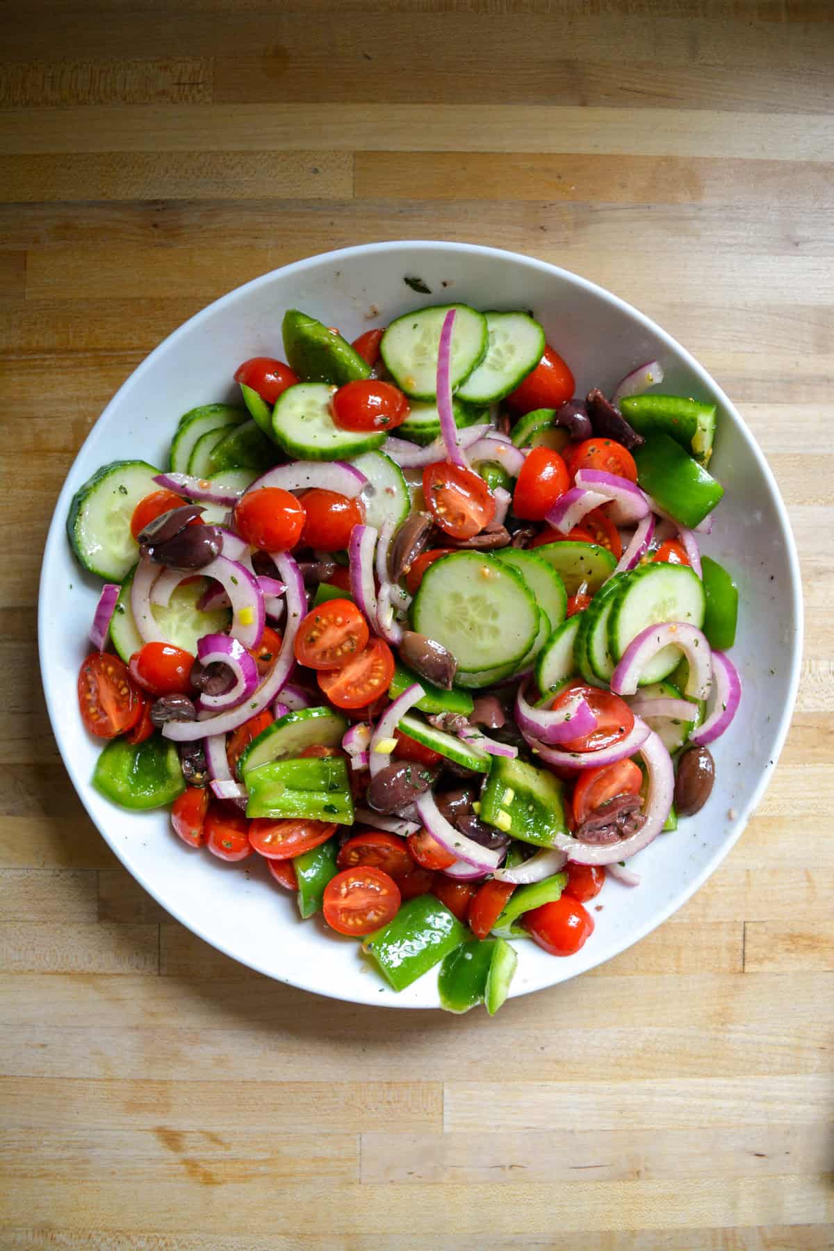 Cucumbers, tomatoes, sliced onion and olives added into the bowl with the dressing.