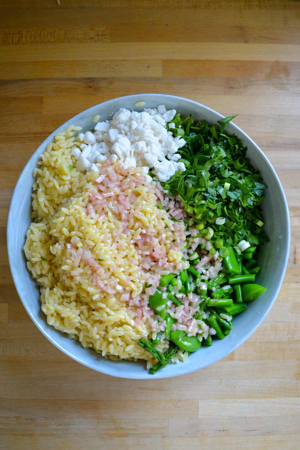 Orzo, lemon dressing, feta cheese and vegetables in a large mixing bowl.