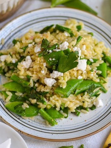 Lemon Orzo Pasta Salad on a plate topped with feta cheese and parsley.