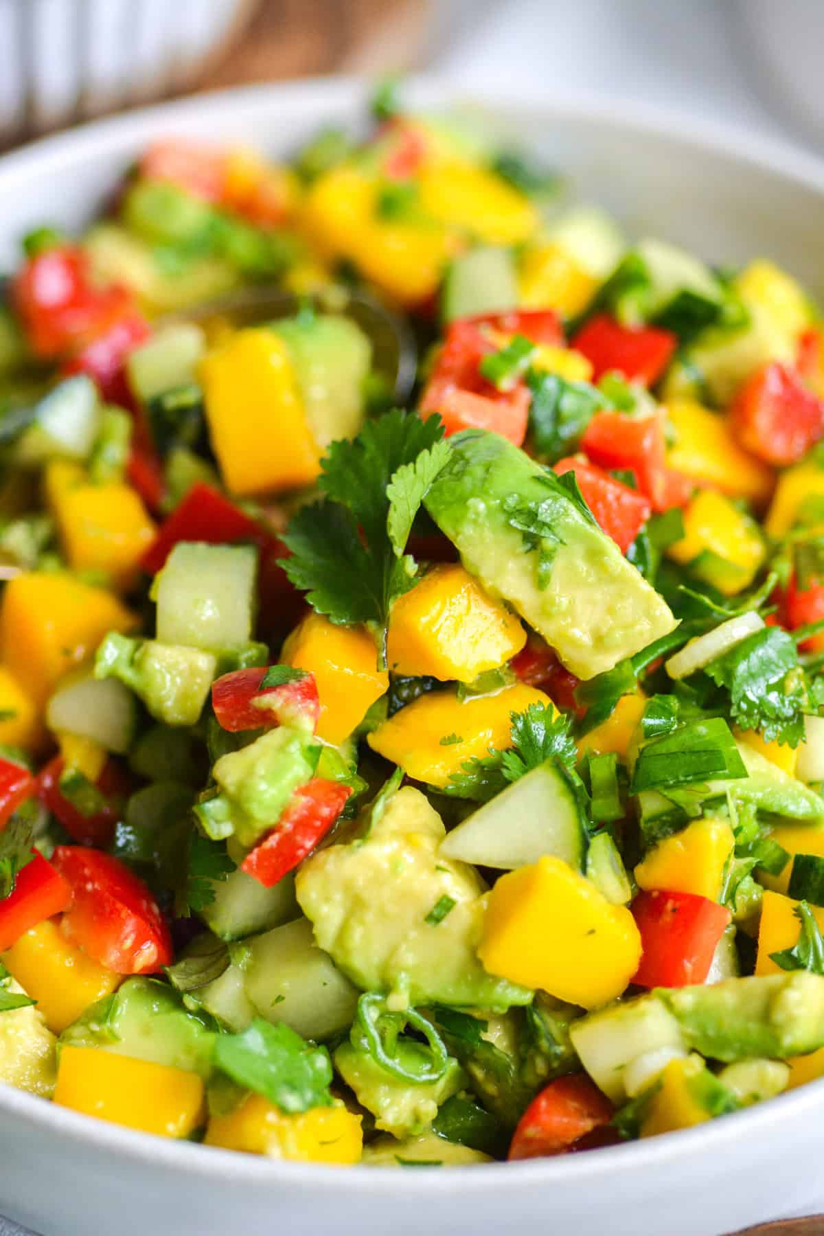 Mango Avocado Cucumber Salad in a bowl topped with a sprig of cilantro.