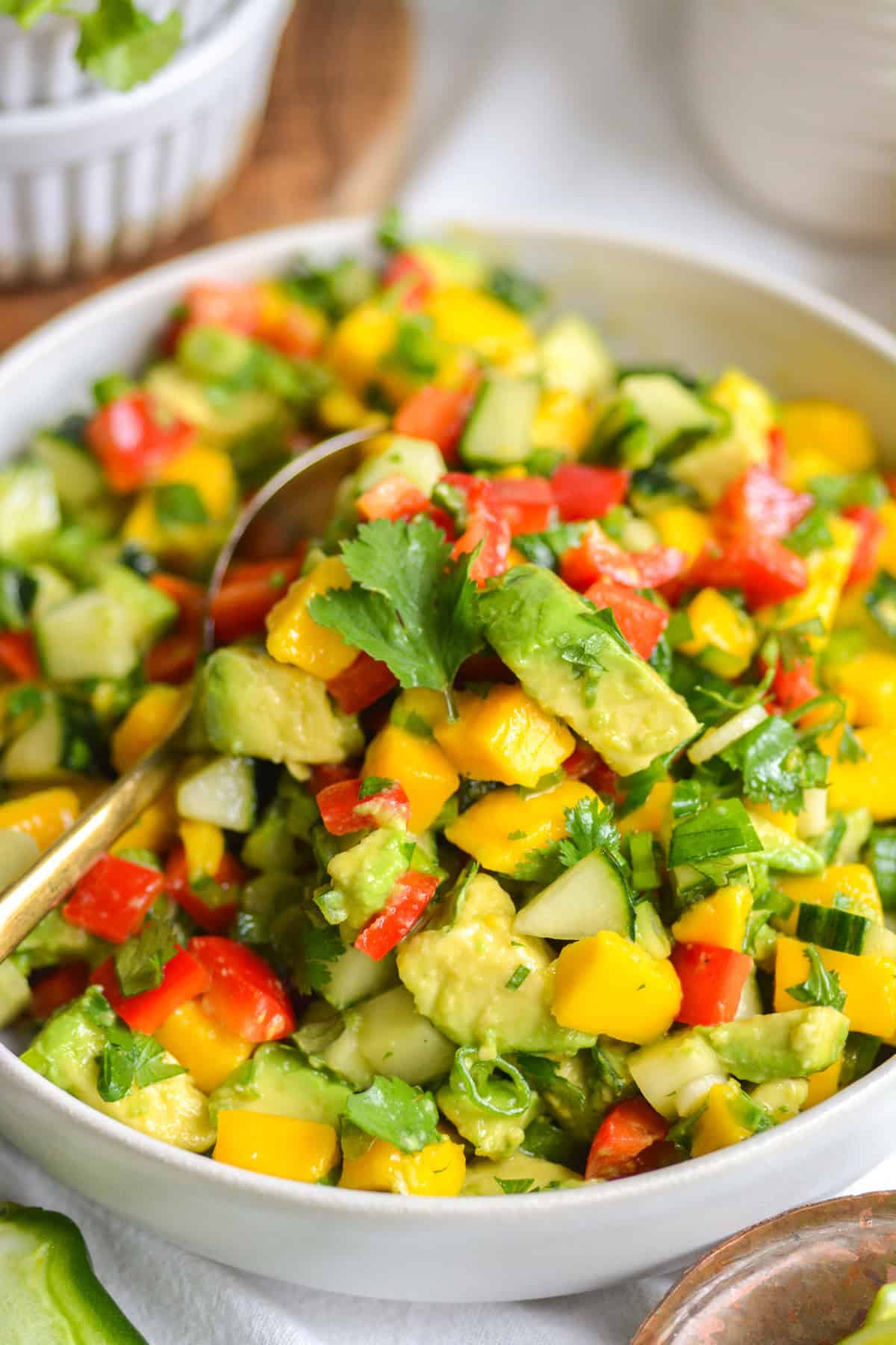 Mango Avocado Cucumber Salad in a bowl with a large spoon in it.