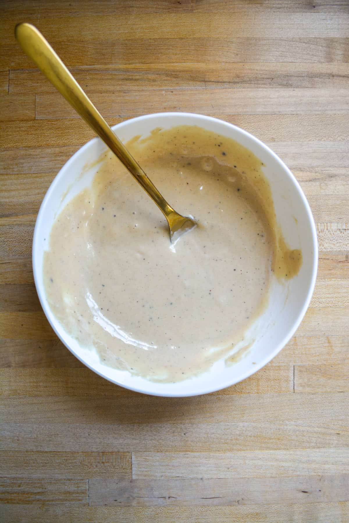 Dressing mixed together in a white bowl on a wooden surface.