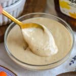 A bowl of Maple Tahini Dressing with a gold spoon in it.