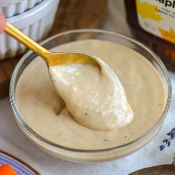 A bowl of Maple Tahini Dressing with a gold spoon in it.