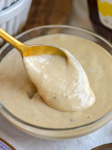 A bowl of Maple Tahini Dressing with a gold spoon in it.