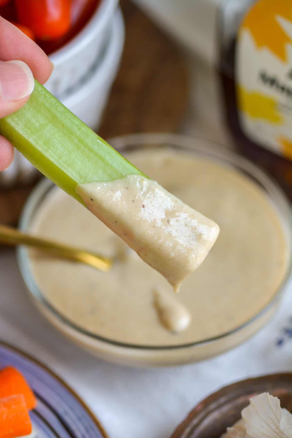 A stick of celery dunked into Maple Tahini Dressing.