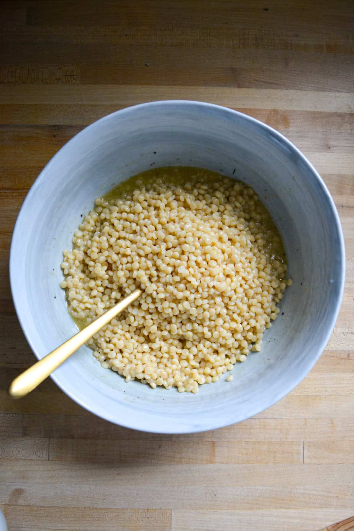 Cooked pearl couscous added to the bowl with vinaigrette in it.