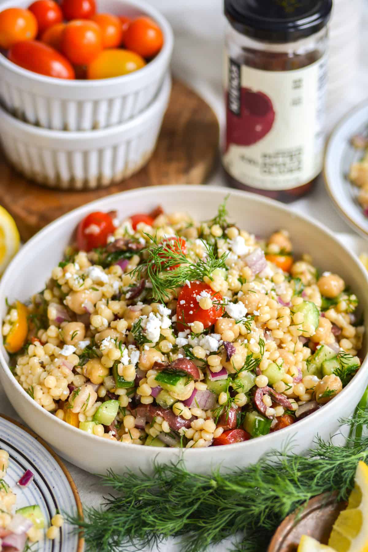 Mediterranean Couscous Salad in a white bowl topped with feta cheese and dill.
