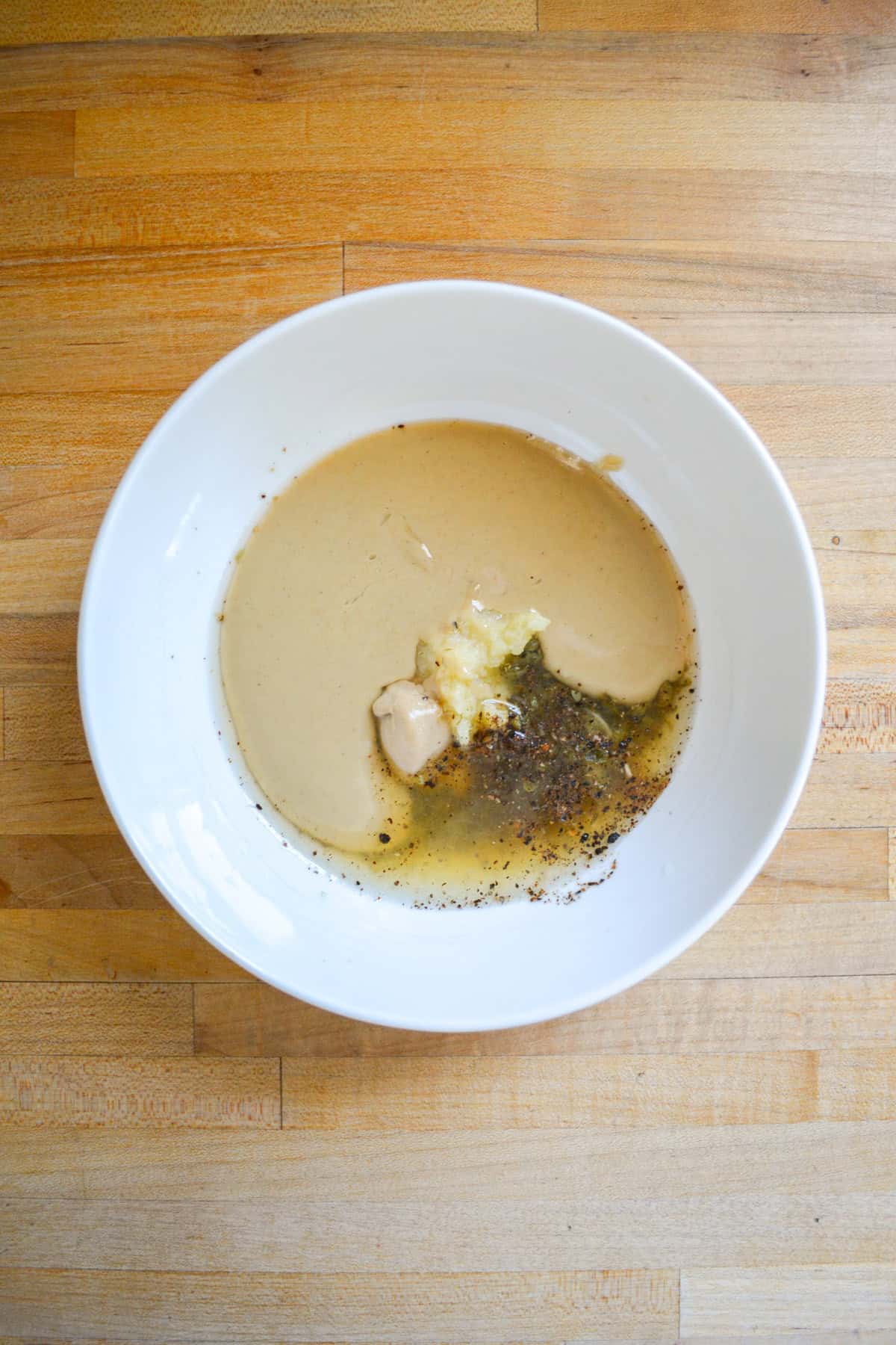 Grated garlic, capers, tahini and lemon juice in a white bowl.
