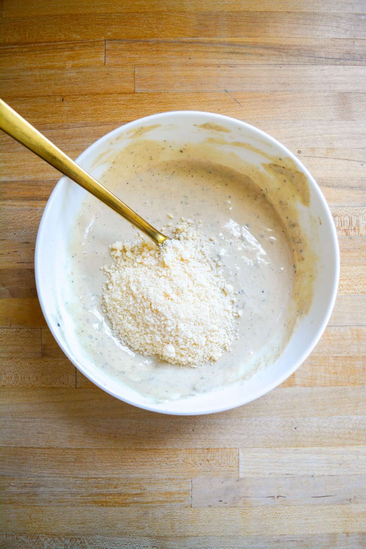 Vegan parmesan cheese added to the creamy dressing in a white bowl.