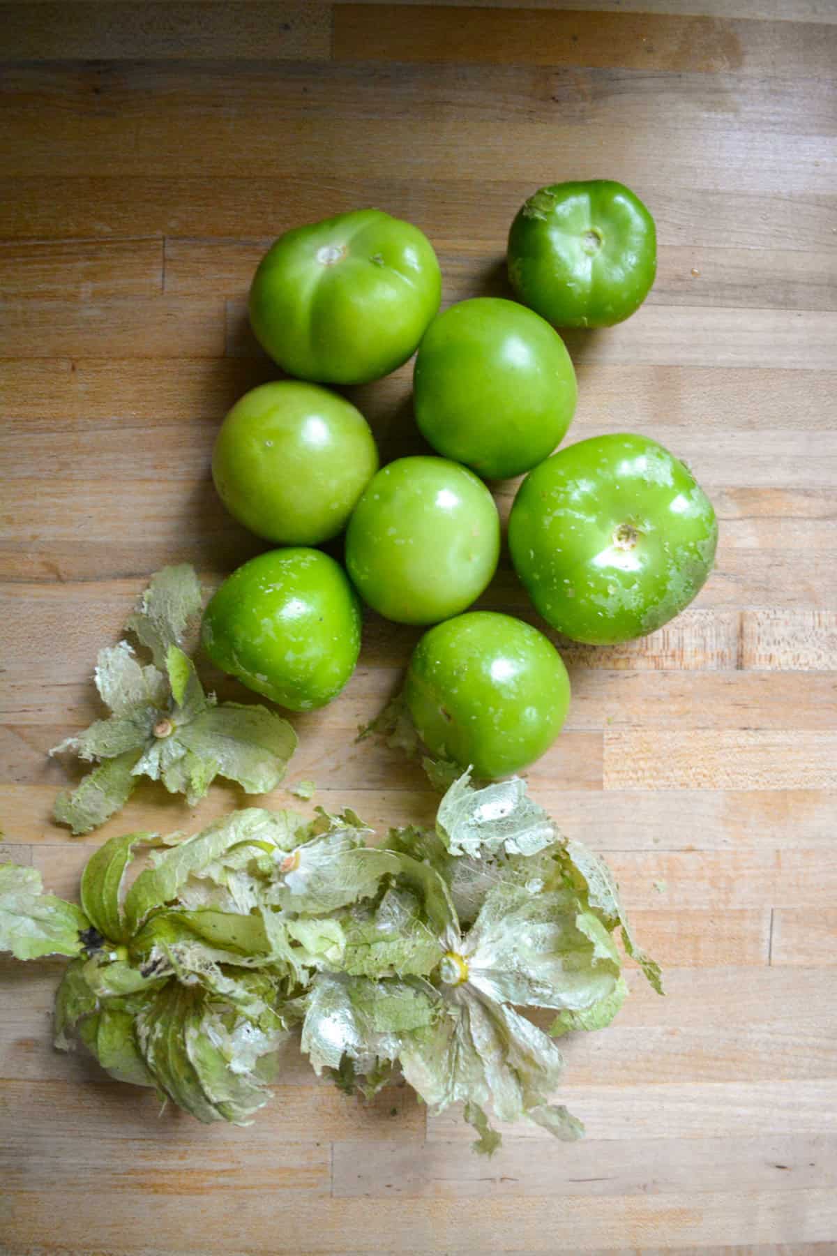  Tomatillos and their papery husks on a wooden surface.