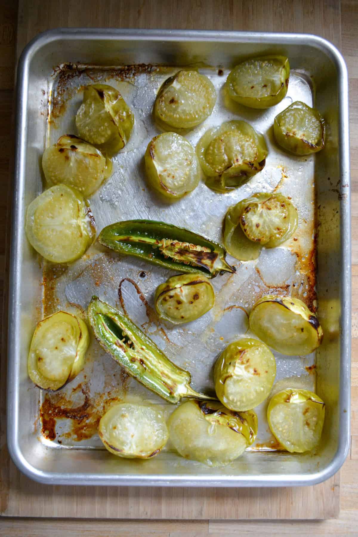 Roasted tomatillos and jalapeños on a baking sheet.