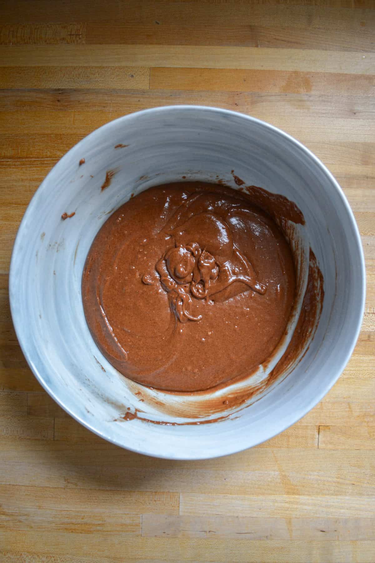 Chocolate batter in a large mixing bowl on a wooden surface.