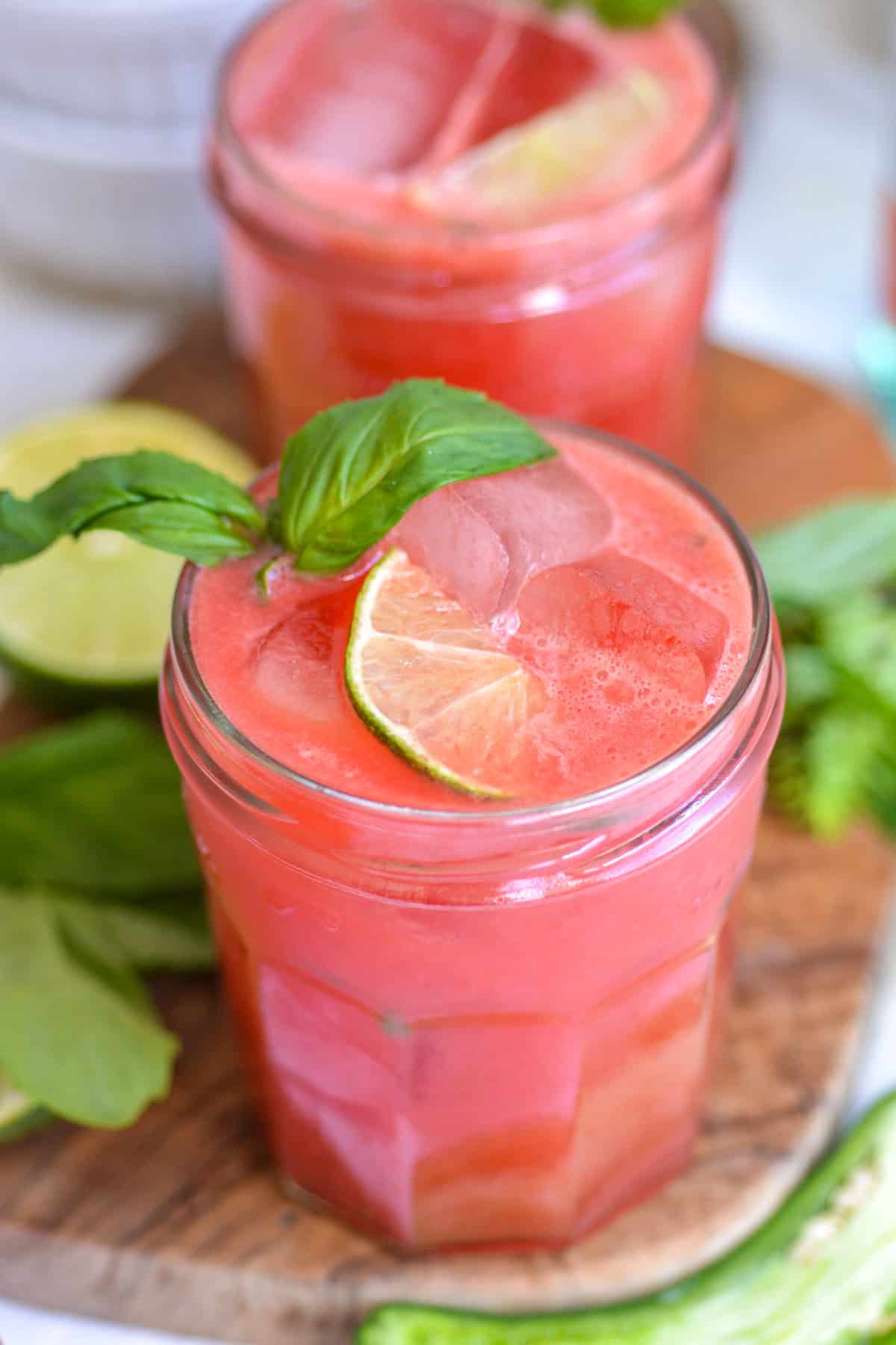Watermelon Vodka Cocktail in a glass topped with a lime and sprig of fresh basil.