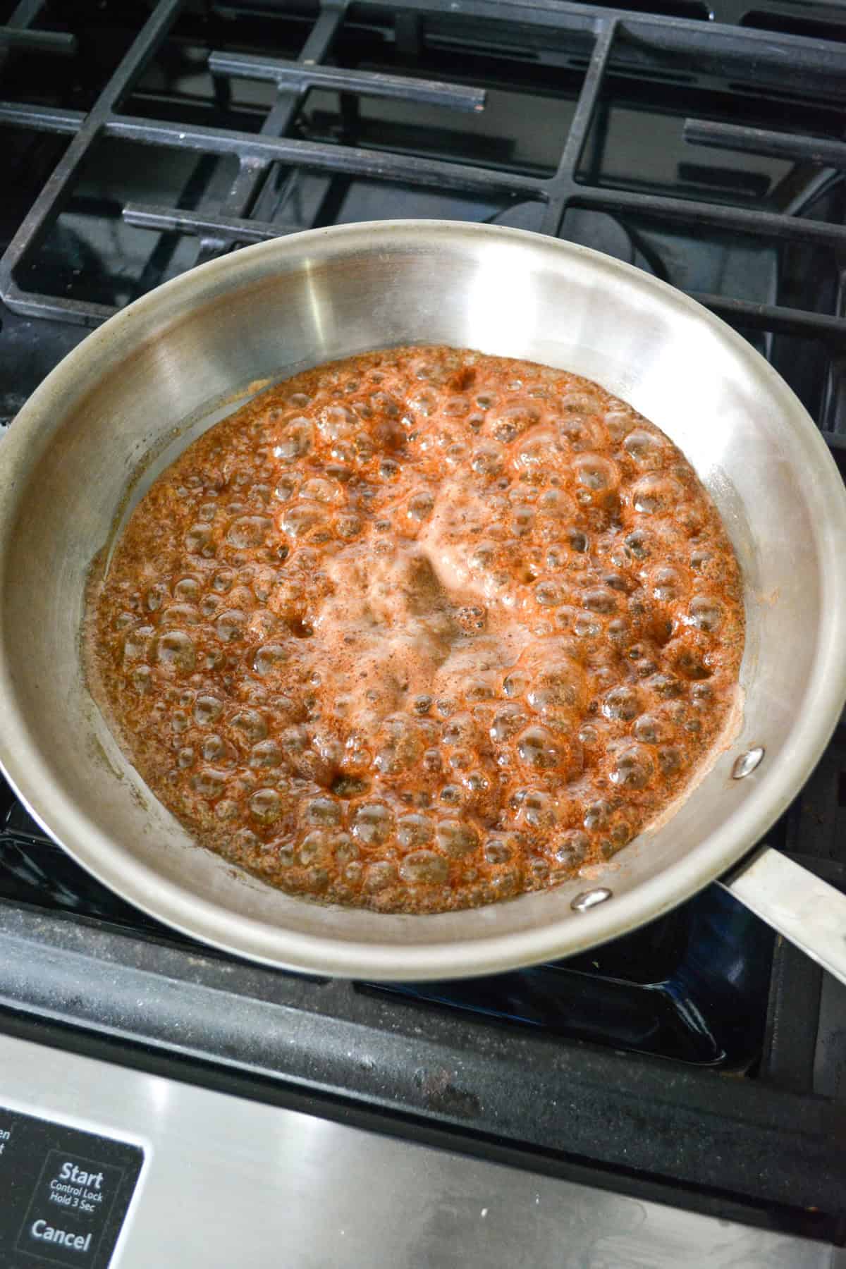 Maple syrup and cinnamon boiling in a skillet.