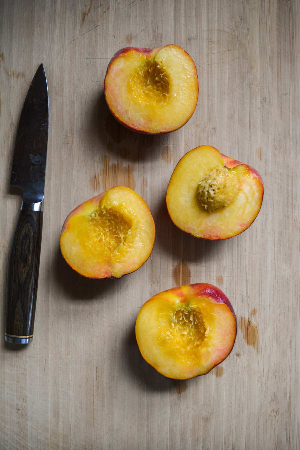 Peaches cut in half on a wooden cutting board.
