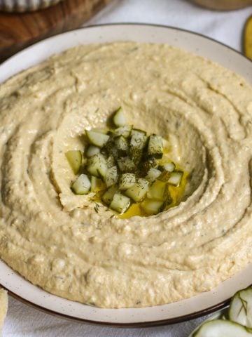 Dill Pickle Hummus on a plate topped with olive oil and chopped pickles.