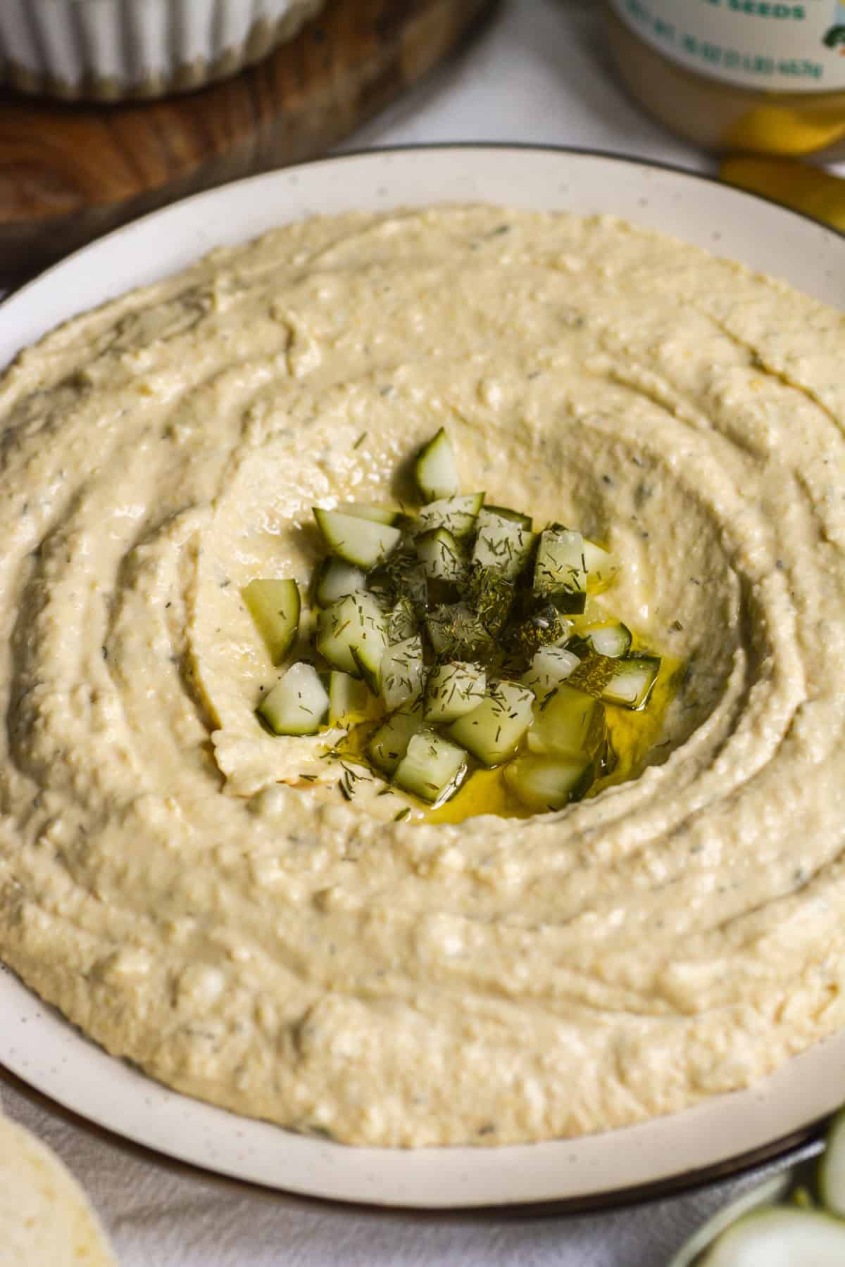 Dill Pickle Hummus topped with olive oil and chopped pickles on a plate.